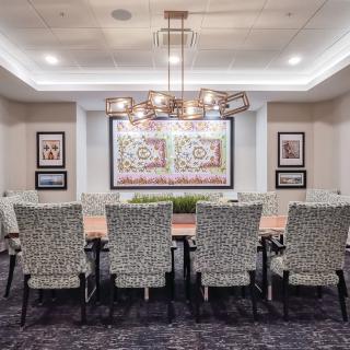 A modern dining room with a long table, patterned chairs, and a decorative chandelier.