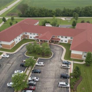 An aerial view of a large building with a red roof, surrounded by a parking lot and greenery.