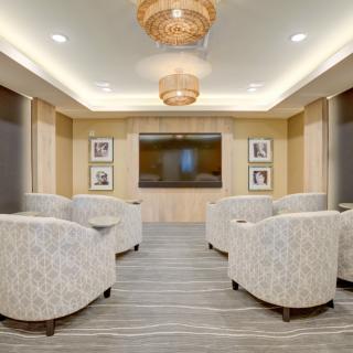 A modern lounge with comfortable seating, chandeliers, and a large television.