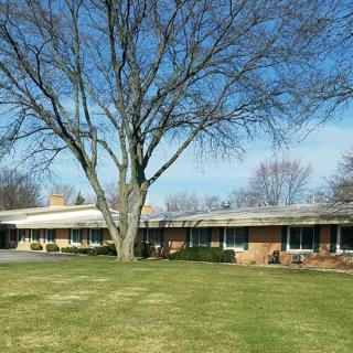 A ranch-style house with a large tree in the front yard, under a clear blue sky.