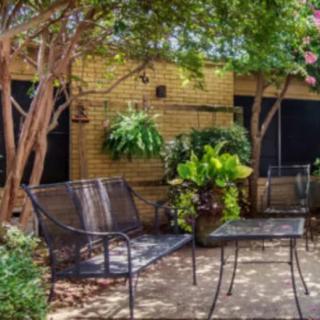 A cozy patio area with metal benches surrounded by lush plants and trees.