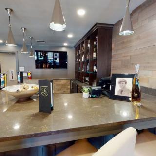 A modern bar setup with a sleek countertop, hanging lights, and a collection of bottles.