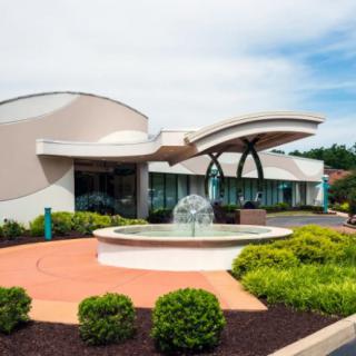 A modern building with a unique curved architecture and a fountain in the foreground, surrounded by landscaped greenery.