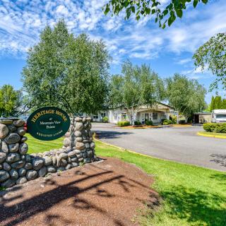 Entrance with a stone wall and sign, surrounded by trees and a driveway.