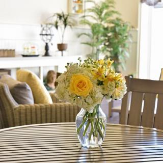 A vase with yellow and white flowers on a wooden table in a cozy living room setting.