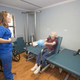 A healthcare professional assists an elderly patient with a therapeutic exercise in a rehabilitation setting.
