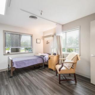 A simple and clean hospital room with a single bed, chair, and large windows.