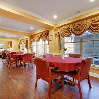 A warmly decorated dining room with red tablecloths, wooden chairs, and large windows adorned with elegant curtains.