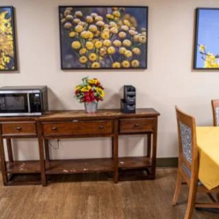 A cozy kitchen setup with wooden furniture, featuring a microwave and coffee maker on a table, alongside vibrant floral artwork on the wall.