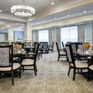 An elegant dining room with neatly arranged tables and chairs, featuring a chandelier and large windows.
