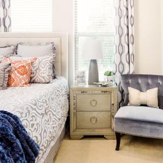 A cozy bedroom with a patterned bedspread, plush chair, and a stylish nightstand.
