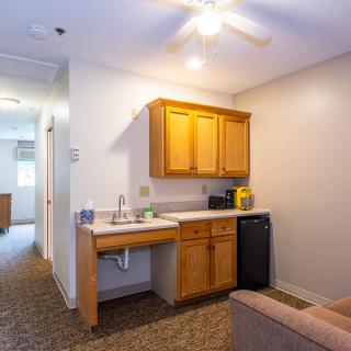 A compact kitchenette in a studio apartment featuring wooden cabinets, a small refrigerator, and essential appliances.