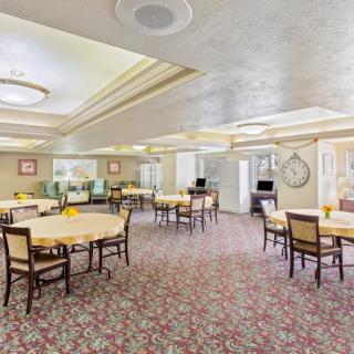 A spacious dining room with several tables and chairs, featuring elegant lighting and a patterned carpet.
