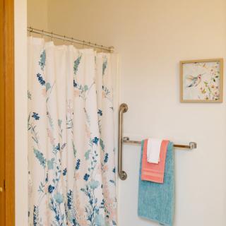 A bathroom with a floral shower curtain, neatly hung towels, and a decorative wall piece.