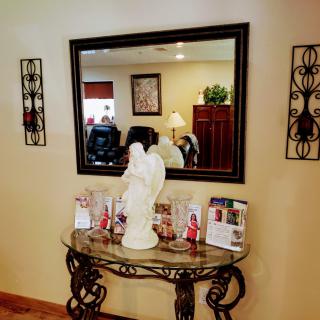 A well-decorated hallway featuring a large mirror, an ornate table, and angel statue surrounded by photographs.