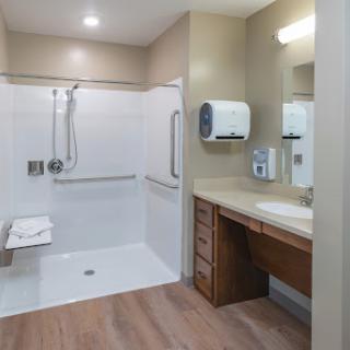 A spacious and modern bathroom designed for accessibility, featuring a shower area and a wooden vanity.