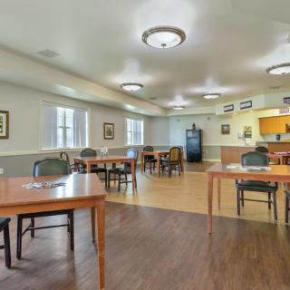 A community dining area with tables and chairs, featuring a wooden floor and modern lighting.