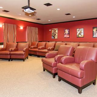 A cozy home theater room with comfortable red seating, a ceiling-mounted projector, and classic movie posters on the walls.