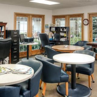 A well-lit office space with tables, chairs, and bookshelves near large windows.
