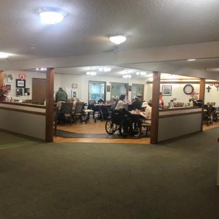 A nursing home community area with elderly residents gathering and engaging in activities.