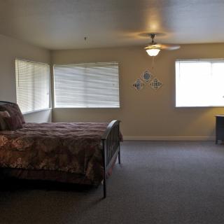 A spacious bedroom with a bed, windows, and a ceiling fan.