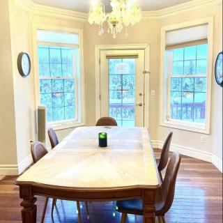 A bright dining room featuring a wooden table with chairs, large windows, and an elegant chandelier.