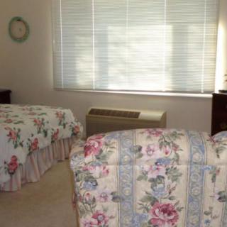 A cozy bedroom with twin beds adorned with floral bedding, illuminated by natural daylight coming through the window.