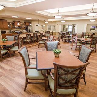 A spacious dining area with neatly arranged tables and chairs, featuring warm lighting and wooden flooring.