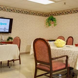 A cozy dining room with neatly arranged tables, chairs, and a television on the wall.