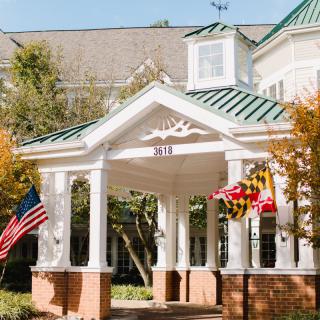 A colonial-style building entrance with American and state flags surrounded by autumn trees.