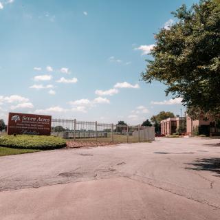 Entrance to a facility with a sign and fencing under a clear sky.