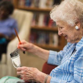 An elderly woman enjoying painting in a library setting.