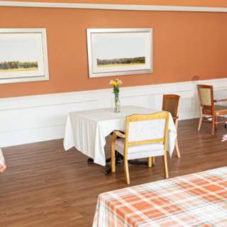 A cozy dining area with neatly arranged tables and chairs, decorated with artwork on the orange walls.