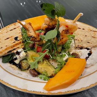 A colorful platter with grilled skewers, fresh salad, mango slices, and flatbread garnish.