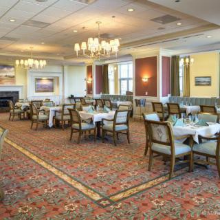 An elegant dining room with neatly arranged tables and chairs, featuring chandeliers and a carpeted floor.