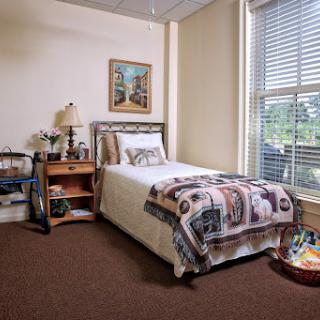 A cozy and well-lit bedroom featuring a single bed, nightstand with a lamp, and decorative items.