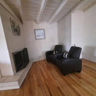 A cozy living room features two black leather chairs facing a fireplace, with artwork on the walls and a wooden floor.