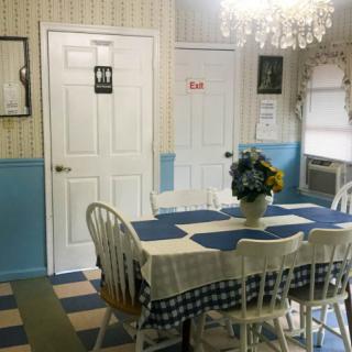 A charming dining room with blue and white decor, featuring a table set with a floral centerpiece, surrounded by chairs and illuminated by a chandelier.