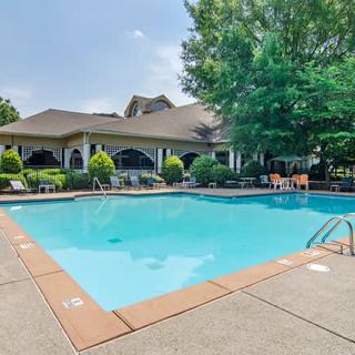 A serene outdoor swimming pool surrounded by trees and a residential patio area.
