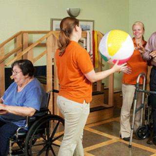 Healthcare workers assist elderly individuals in a physical therapy session using a beach ball.