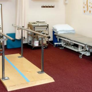 A therapy room equipped with parallel bars and a treatment table for rehabilitation exercises.