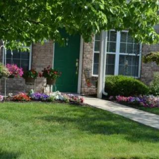 A well-maintained front yard with a variety of colorful flowers and green grass leading up to a house.