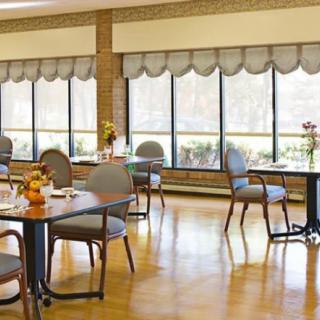 A bright dining room with tables and chairs arranged near large windows.