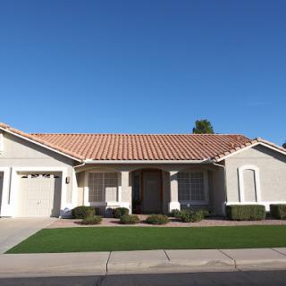 A charming single-family home with a tiled roof and neat landscaping under a clear blue sky.