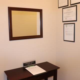 An office corner featuring a mirror, a small table with documents, and framed certificates on the wall.