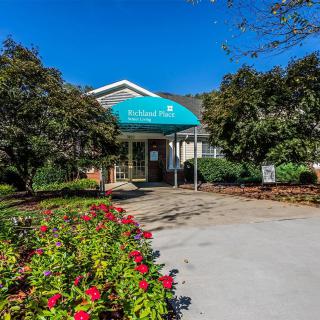 A sunny view of a building entrance with an awning, surrounded by a garden and pathway.