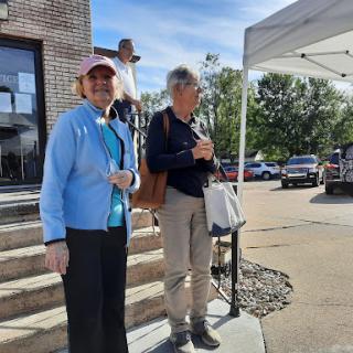 Two individuals standing outside at an event, enjoying a sunny day.