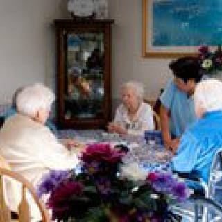 A group of elderly individuals sitting together, possibly in a care home setting, engaged in conversation.