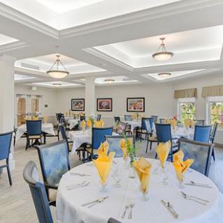 An elegant dining room with round tables set for a meal, featuring yellow napkins and blue chairs.