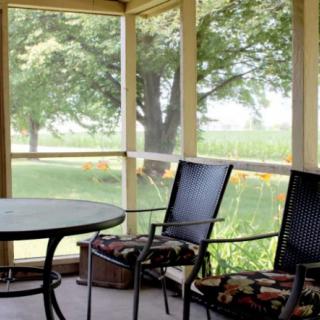 A serene screened porch with chairs and a table overlooking lush greenery.